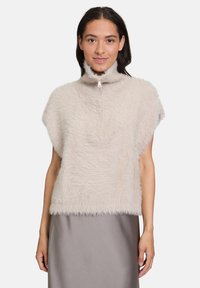 Faux-Fur-Weste in hellem Beige mit hohem Kragen, kurzen Ärmeln und partiellem Reißverschluss vorne. Weiche Textur mit flauschigem Aussehen.