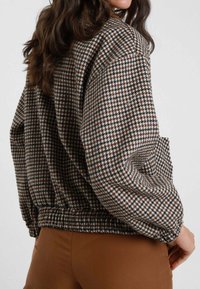 Giacca con motivo houndstooth marrone e crema, dotata di cintura elastica, spalle scese e tessuto texturizzato. Vista posteriore mostrata.