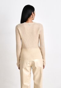 Maglione a coste beige con maniche lunghe, vita aderente e scollatura rotonda, abbinato a pantaloni chiari, lucidi e a vita alta.