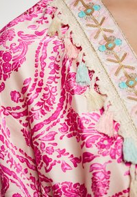 Kimono in seta con un intricato motivo floreale rosa su uno sfondo chiaro. Presenta ricami decorativi e nappine colorate lungo i bordi.