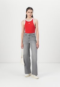 Rotes, geripptes Tanktop mit weißem Besatz und "GAP"-Logo, kombiniert mit hoch taillierten, grauen, weiten Jeans und weißen Sneakers. Kleine Schultertasche.