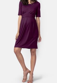 Burgundy graviddress med figursydd överdel, korta ärmar och en flödande kjol som går under knäna. Slät tyg med en subtil lyster.