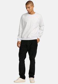 Light gray sweatshirt with raglan sleeves and ribbed cuffs, paired with black pants and white sneakers. Simple design, no visible logos.