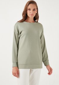 Sudadera de manga larga verde claro, hecha de una tela suave, con un corte relajado, un escote amplio y puños acanalados.