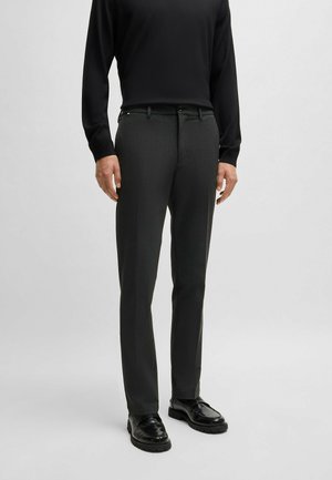 Mörkgrå dressbyxor med en subtil textur, rak bendesign, snedställda fickor och knappstängning. Tillsammans med en svart skjorta med långa ärmar.