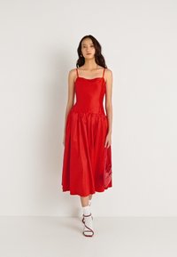 Κόκκινο αμάνικο φόρεμα με εφαρμοστό κορσέ και πλήρη φούστα. Φτιαγμένο από λείο ύφασμα; περιλαμβάνει λεπτές τιράντες και κυματιστό ντεκολτέ.