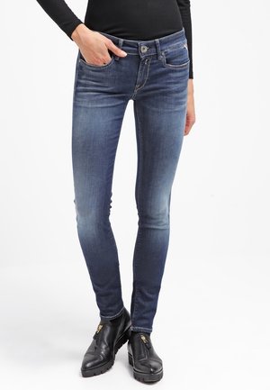 Jeans ajustados de denim, con un lavado azul oscuro, diseño de cinco bolsillos y cierre de cremallera. Acentuados con un botón de metal.