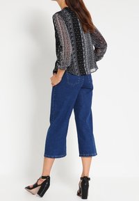 Blusa de estampado en blanco y negro con mangas largas, combinada con culottes de mezclilla azul de tiro alto y sandalias negras de tacón alto.