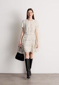 Īsām piedurknēm, krēmkrāsas kleita ar teksturētām svītrām, valkāta kopā ar ceļgala augstiem melniem zābakiem un mazu, savilktu melnu rokassomu.