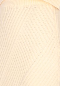 Crème gebreide stof met een textuurpatroon van diagonale ribbels. Het oppervlak lijkt zacht met variërende diktes in het garen.