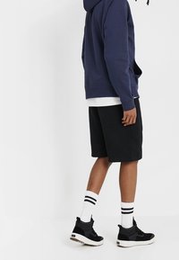 Námořnická mikina, černé šortky, bílý tričko pod tím. Černé tenisky s bílými a černými pruhovanými ponožkami. Pohodlný sportovní outfit.