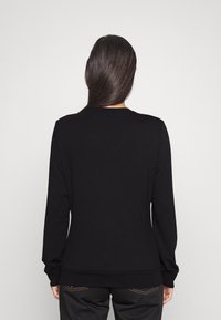 Zwarte sweatshirt met lange mouwen, ronde hals en een aansluitende tailleband. Zachte stoffen textuur en minimalistisch ontwerp. Geen zichtbare logo's of patronen.