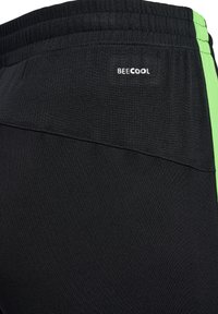 Gros plan sur un pantalon de sport noir avec des panneaux texturés, une taille élastique, le logo "BEE COOL" et une bande latérale vert néon.