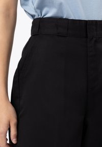 Svarta tygbyxor med en slät textur, iögonfallande midjeband, sidofickor och rak benmodell.