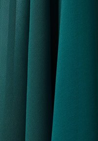 Teal- und dunkelgrüne, strukturierte Stofffalten, die vertikal hängen, mit subtilen Licht- und Schattenkontrasten.