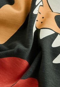 Černá látka s živým červeným kruhem a designem kreslené postavičky, která má bílé zuby a krémové akcenty, měkký texturovaný materiál.