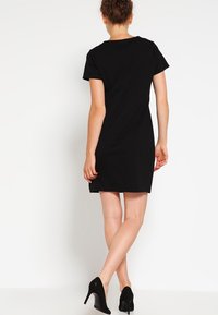 Czarna sukienka z krótkim rękawem wykonana z gładkiego materiału, z okrągłym dekoltem i prostym krojem, w połączeniu z czarnymi szpilkami.