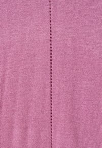 Gros plan sur un tissu tricoté rose avec une rangée verticale de petits trous ajourés uniformément espacés courant au centre.