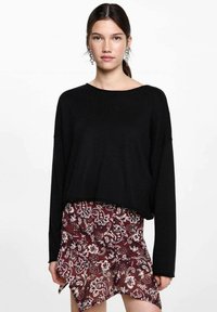 Schwarzer, übergroßer Pullover mit langen Ärmeln, kombiniert mit einem bordeauxfarbenen Rock mit Muster, der Blumen- und Paisleymuster aufweist und einen gerafften Saum hat.