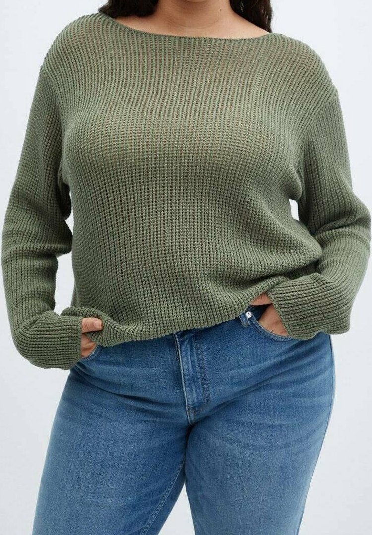 Groene, chunky gebreide trui met een wijde halslijn en lange mouwen; gedragen met strakke blauwe jeans, die een relaxte pasvorm en gestructureerd patroon tonen.