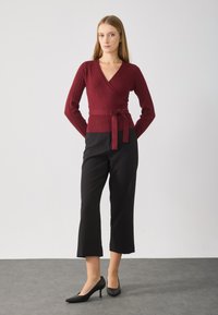 Top envolvente ribbed bordeaux com mangas longas, atado na cintura, combinado com calças pretas curtas e sapatos de salto agudo pretos.