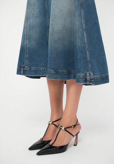 Pantofi cu toc slingback din piele patent neagră, cu vârf ascuțit, accente din metal aurit și un toc subțire, de înălțime medie. Purtați cu o fustă din denim.