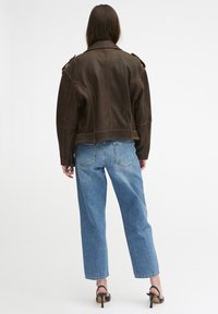Braune Lederjacke mit sichtbaren Nähten, Schulterklappen und einem verkürzten Schnitt, kombiniert mit hellblauen hochgeschnittenen Jeans.