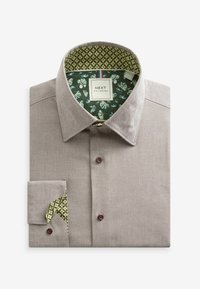 Cămașă cu model maro deschis, cu guler, având un interior din material floral verde și butoane contrastante. Textura generală este netedă.