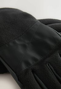 Schwarze Handschuhe aus weichem Fleece-Material mit einem glatten, glänzenden schwarzen Stoffeinsatz und strukturierten Griffen an den Fingern.