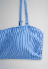 Világoskék bordázott crop top vékony, állítható vállpántokkal, szürke háttéren.