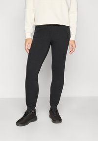 Černé teplákové kalhoty s úzkým střihem, elastickým pasem a žebrovanými lemy, spojené s krémovou mikinou a černými teniskami.