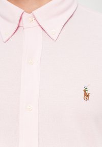 Svetloružová polo tričko s textúrovanou tkaninou, s klasickým golierom, zapínaním na gombíky a malým vyšívaným logom koňa a jazdca.