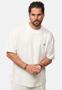 Weißes Baumwoll-T-Shirt mit kurzen Ärmeln und rundem Halsausschnitt, mit einem kleinen mehrfarbigen Logo auf der linken Brust.