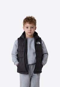 Svart dunvest med hette, med glidelåslukking og sidelommer, brukt over en lys grå hettegenser og matchende joggebukser.