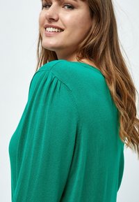 Grüner Pullover mit lockerer Passform, ausgestattet mit Raffung an den Schultern und einer glatten Textur. Weiches, leichtes Strickmaterial.