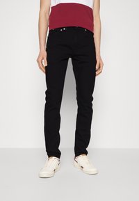 Jeans negros ajustados en material de denim, con cinco bolsillos y cierre de botón metálico. Combinados con una camiseta a rayas en color burdeos y blanco.