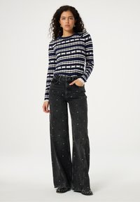 Marineblauw en wit gestreepte ribbel trui met lange mouwen, gecombineerd met zwarte wijde jeans met zilveren stippenversieringen. Casual outfit met een losse pasvorm.