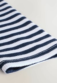 Tissu rayé bleu marine et blanc, texture côtelée, avec un bord replié montrant une couture propre. Le motif alterne entre de larges et étroites rayures.