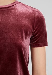 Burgundy sammet t-shirt med kort ärm som har en mjuk yta, en lätt glans och en åtsittande design. Rund halsringning med färdiga fållar.