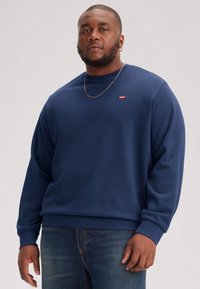 Navy blue sweatshirt made of soft fabric with a round neckline, ribbed cuffs, and a small red logo on the left chest.