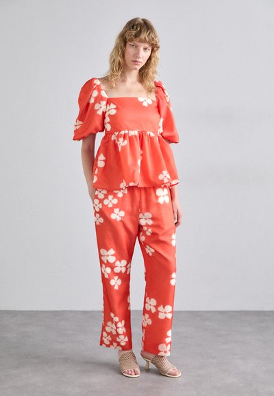 Rød blomstret peplum-topp og matchende bukser, med pufferm og hvite blomstermønstre. Bært med beige hælede sandaler.