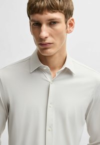 Lichtgrijze shirt met patroon, een gespreide kraag, subtiele textuur en een sluiting met knopen aan de voorkant. Heeft een slim fit ontwerp en stevige knopen.