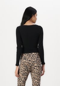 Crni rebrasti dugih rukava s obodnom izrezom, uparen s uskim hlačama sa leopard uzorkom. Tkanina izgleda mekano s teksturiranim završetkom.