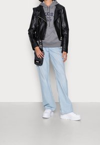 Giacca da biker in pelle nera sopra felpa grigia, jeans a vita alta blu chiaro e sneakers bianche chunky. Piccola borsa a tracolla nera con dettagli a fantasia.