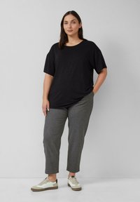 Czarny t-shirt o luźnym kroju z krótkimi rękawami, w zestawieniu z szarymi dopasowanymi spodniami i białymi trampkami z beżowymi akcentami. Widoczna gładka struktura tkaniny.