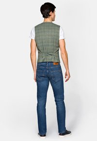 Zielona kamizelka w kratkę o dopasowanym kroju, z tylnym wiązaniem. Połączona z niebieskimi dżinsami i jasnymi trampkami.