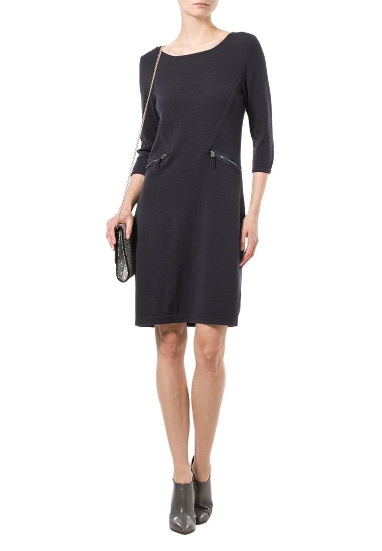 Abito a maglia colore navy con maniche a tre quarti, dotato di due tasche con zip. La modella tiene in mano una borsa metallica piccola e indossa stivaletti grigi alla caviglia.