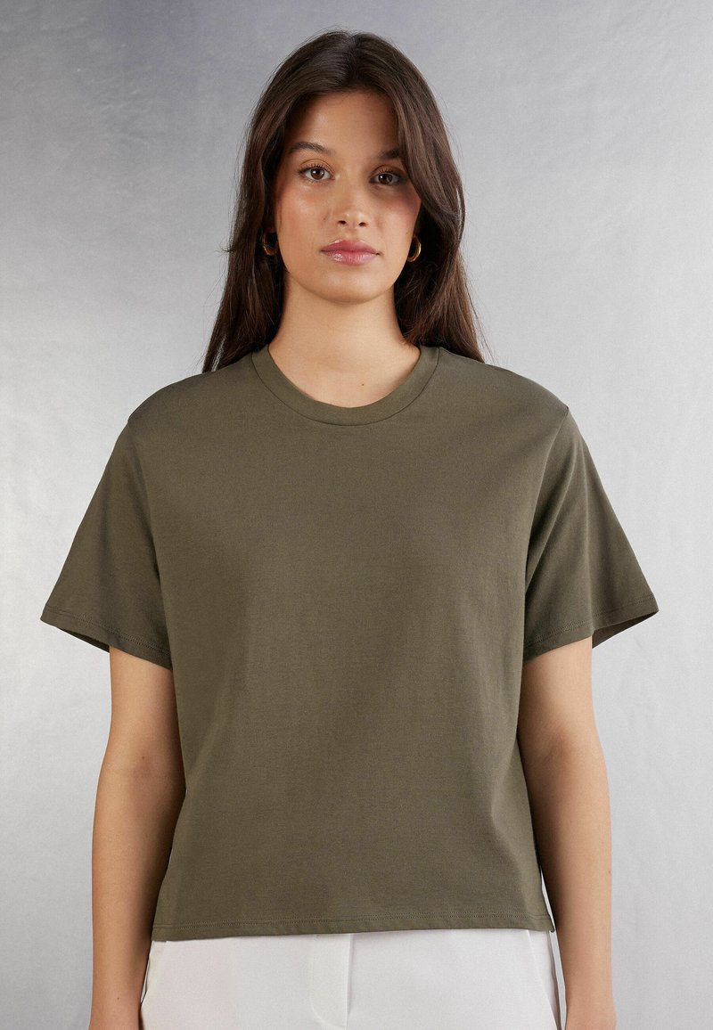 Olivgrön bomulls t-shirt med korta ärmar, rund halsringning och avslappnad passform. Slät textur, inga synliga mönster eller detaljer.
