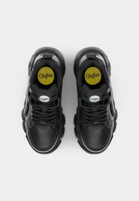 Zwarte leren sneakers met dikke zolen, ronde neuzen en platte veters. Zwarte accenten en een geel logo op de binnenzool. Eenvoudig, modern ontwerp.