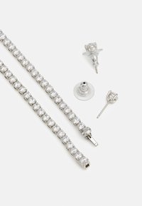 Zilverkleurige armband en oorbellen met ronde, transparante kristallen in een klauwzetting. De armband heeft een sluiting; de oorbellen hebben een stud-achterkant en accenten.